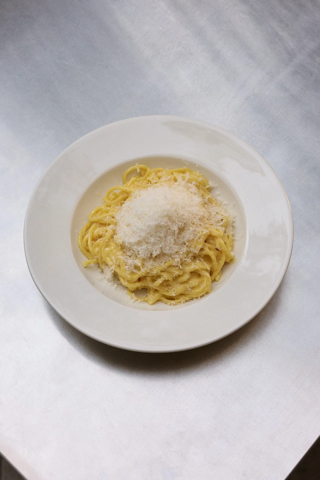 A plate of spaghetti with grated cheese, seen from above