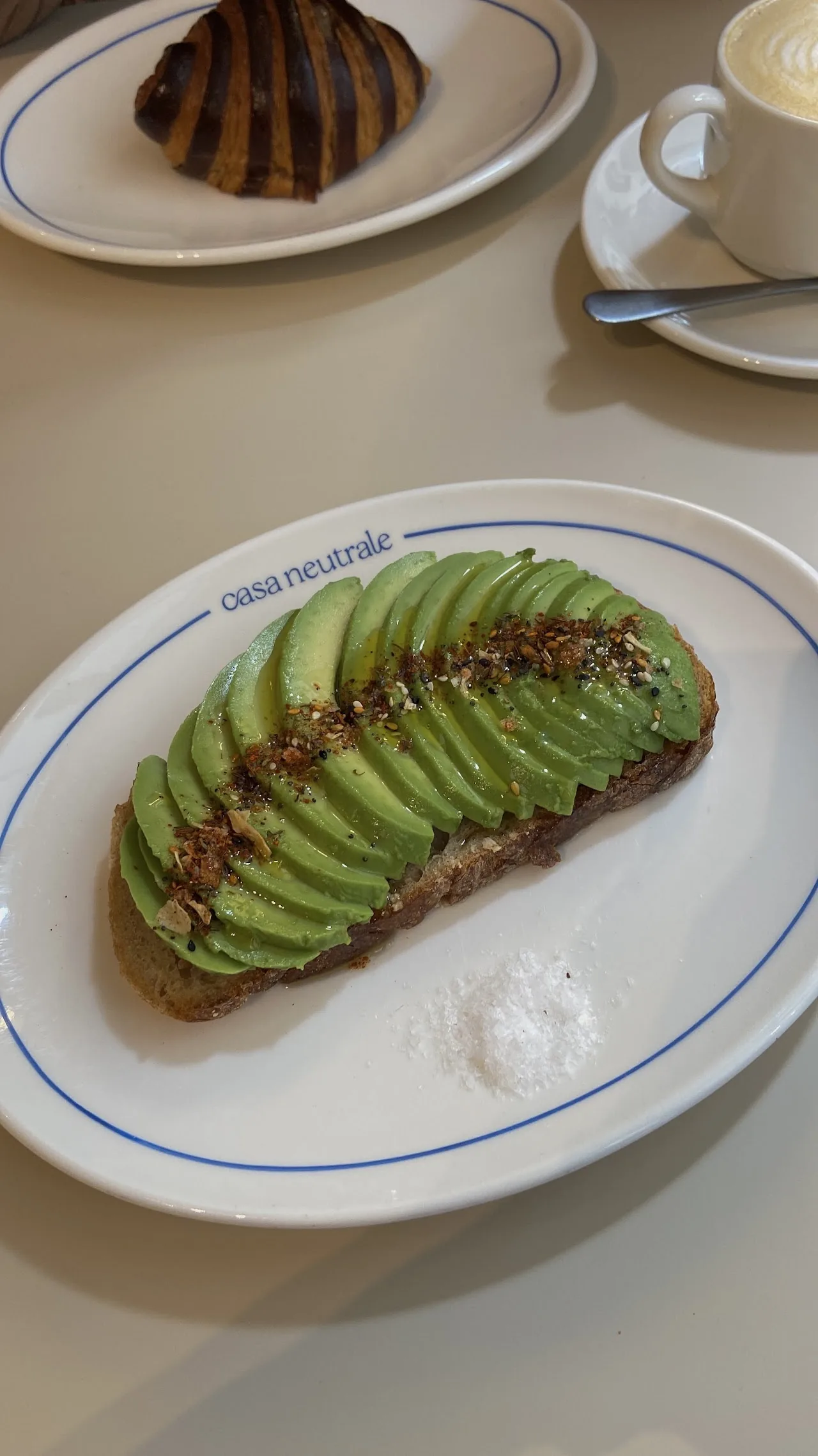 Sliced avocado toast on a plate beside a pastry and coffee