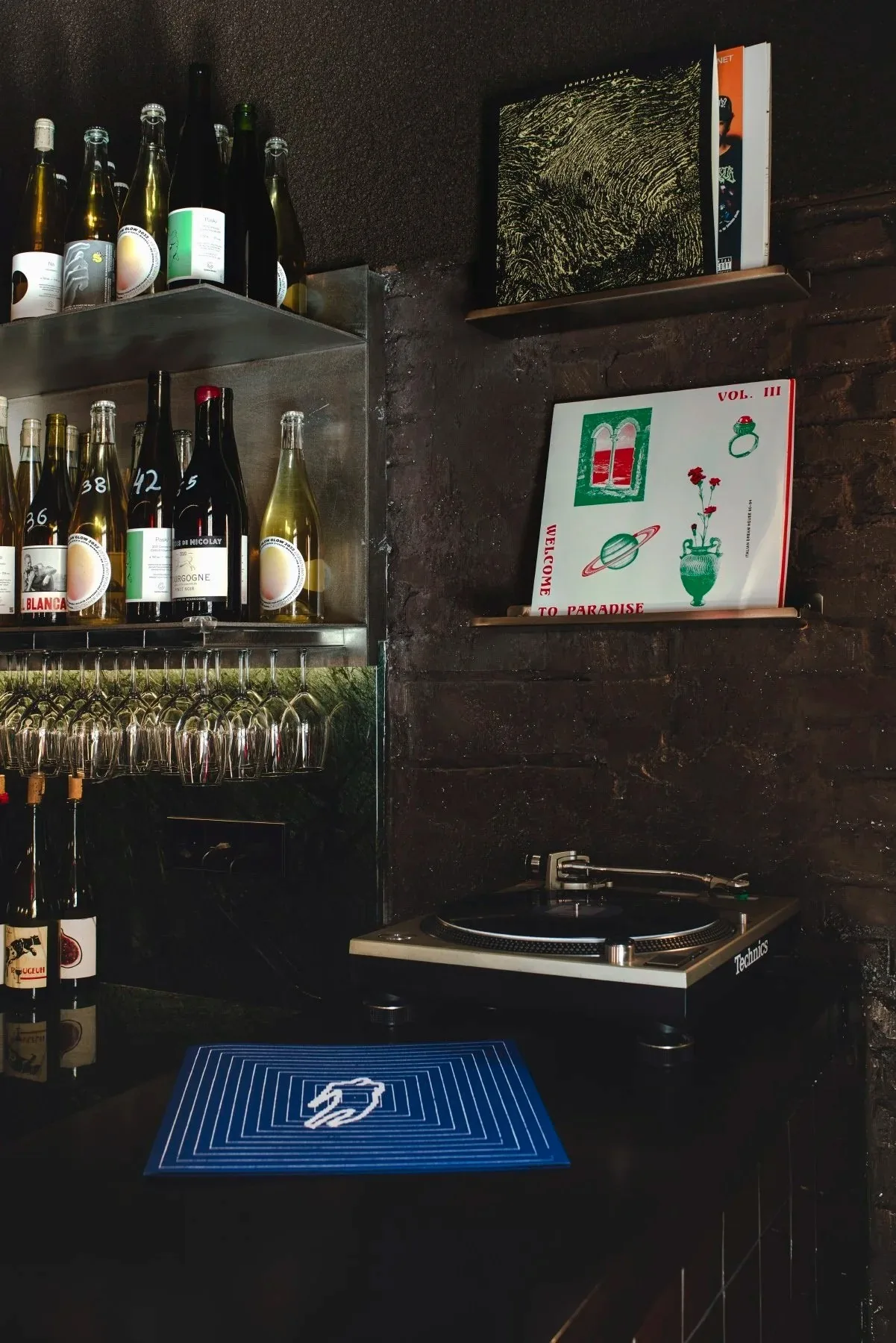 A record player on a shelf beside rows of wine bottles and glasses