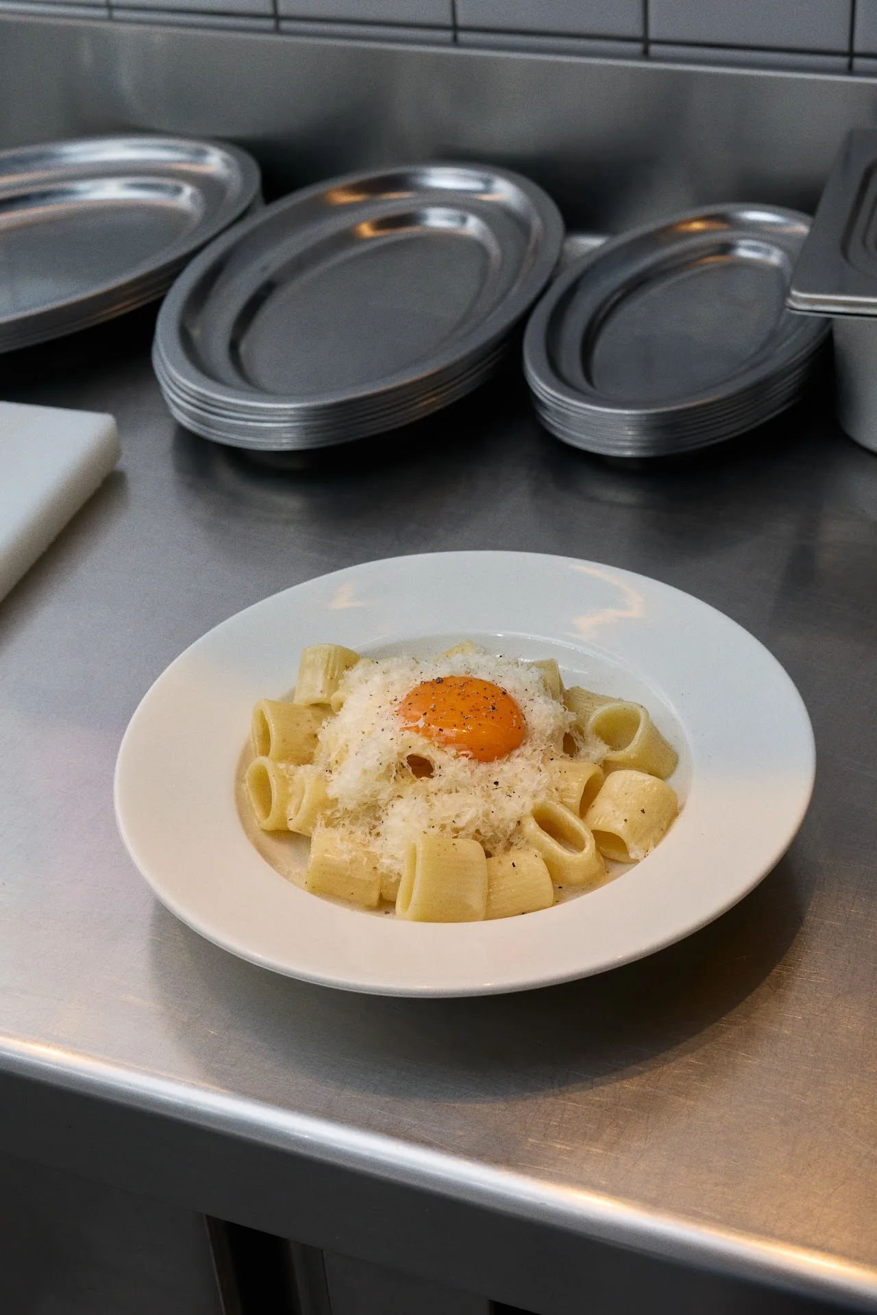 A plate of pappardelle pasta topped with a raw egg yolk and grated cheese