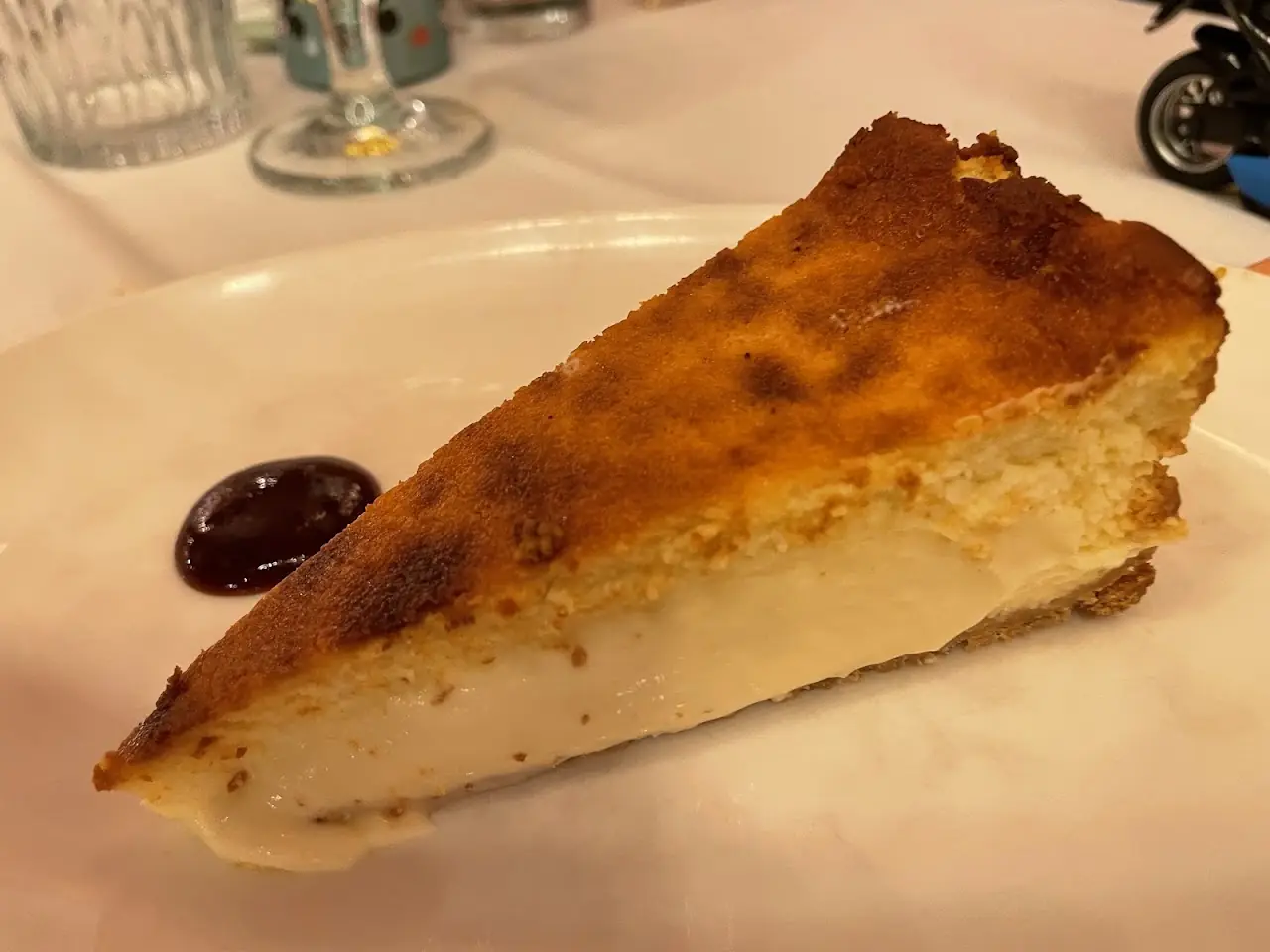 A slice of baked cheesecake with a caramelized top, served with a small pool of berry sauce.