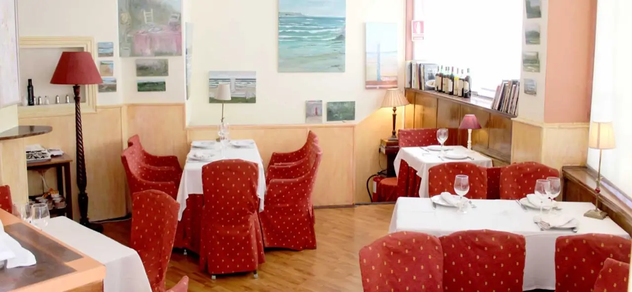 Classic dining room with red polka-dot chair slipcovers, white-linen tables, coastal seascape paintings on the walls and lamp-lit wooden wainscoting