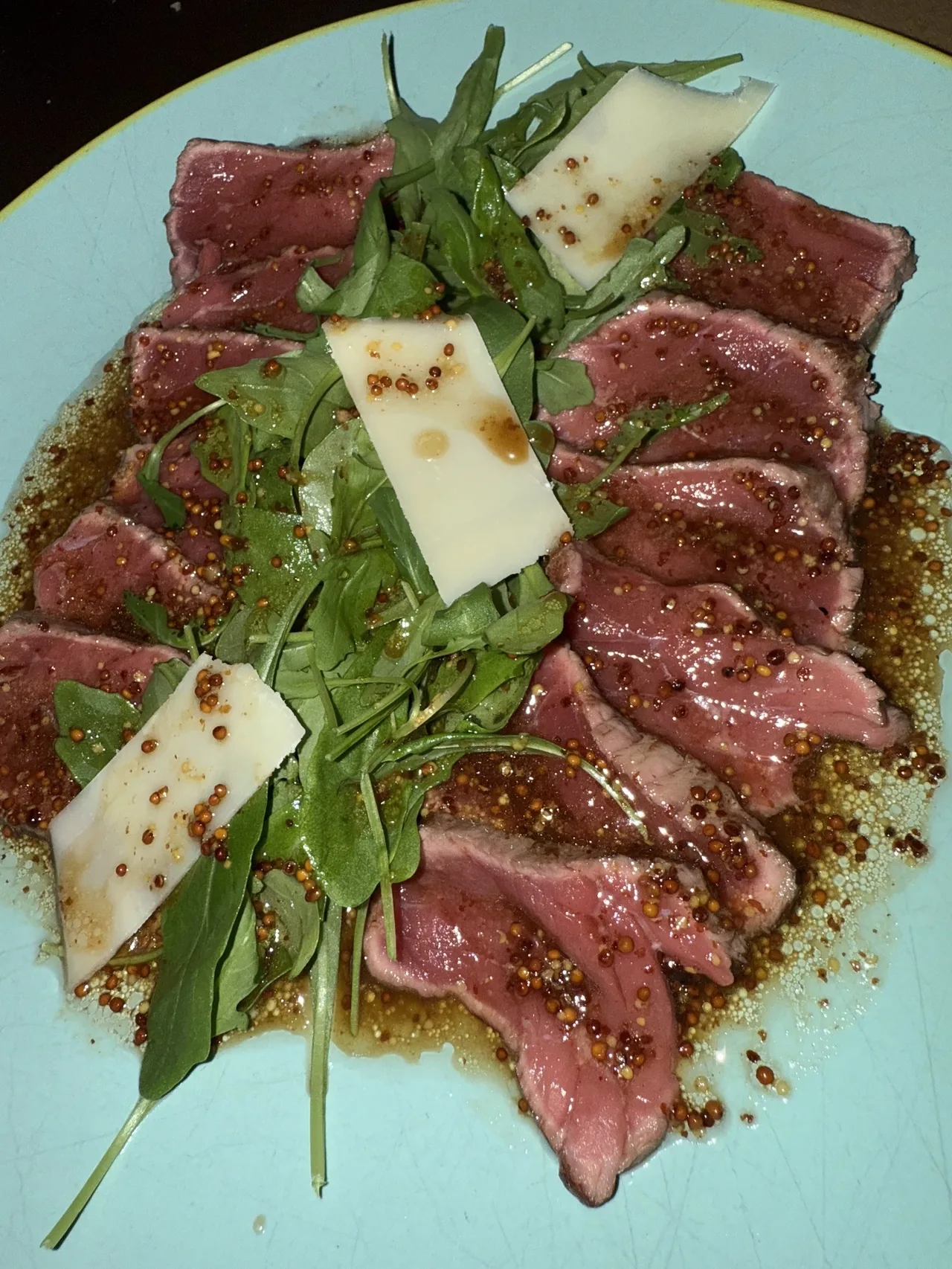 Slices of rare beef with rocket leaves and shavings of cheese on a pale plate