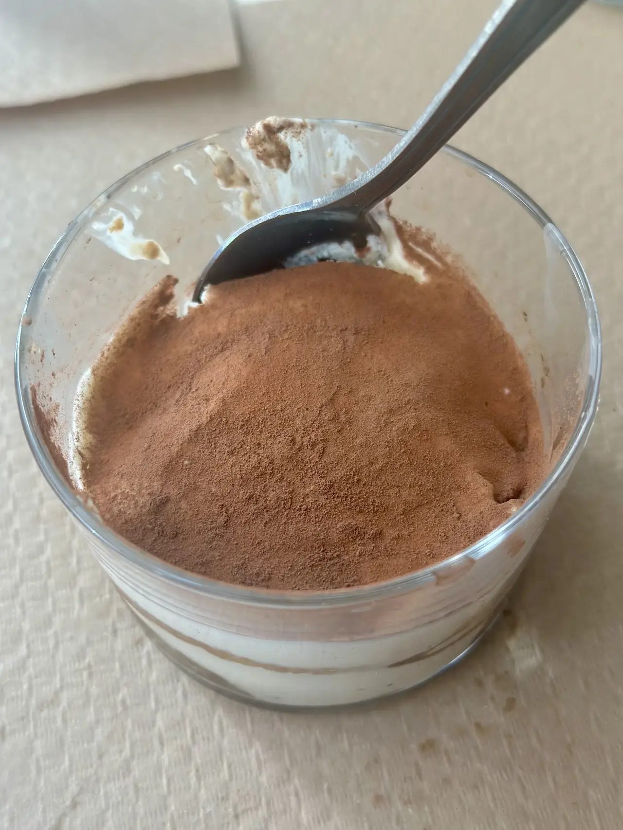 A glass of tiramisu dusted with cocoa, with a spoon