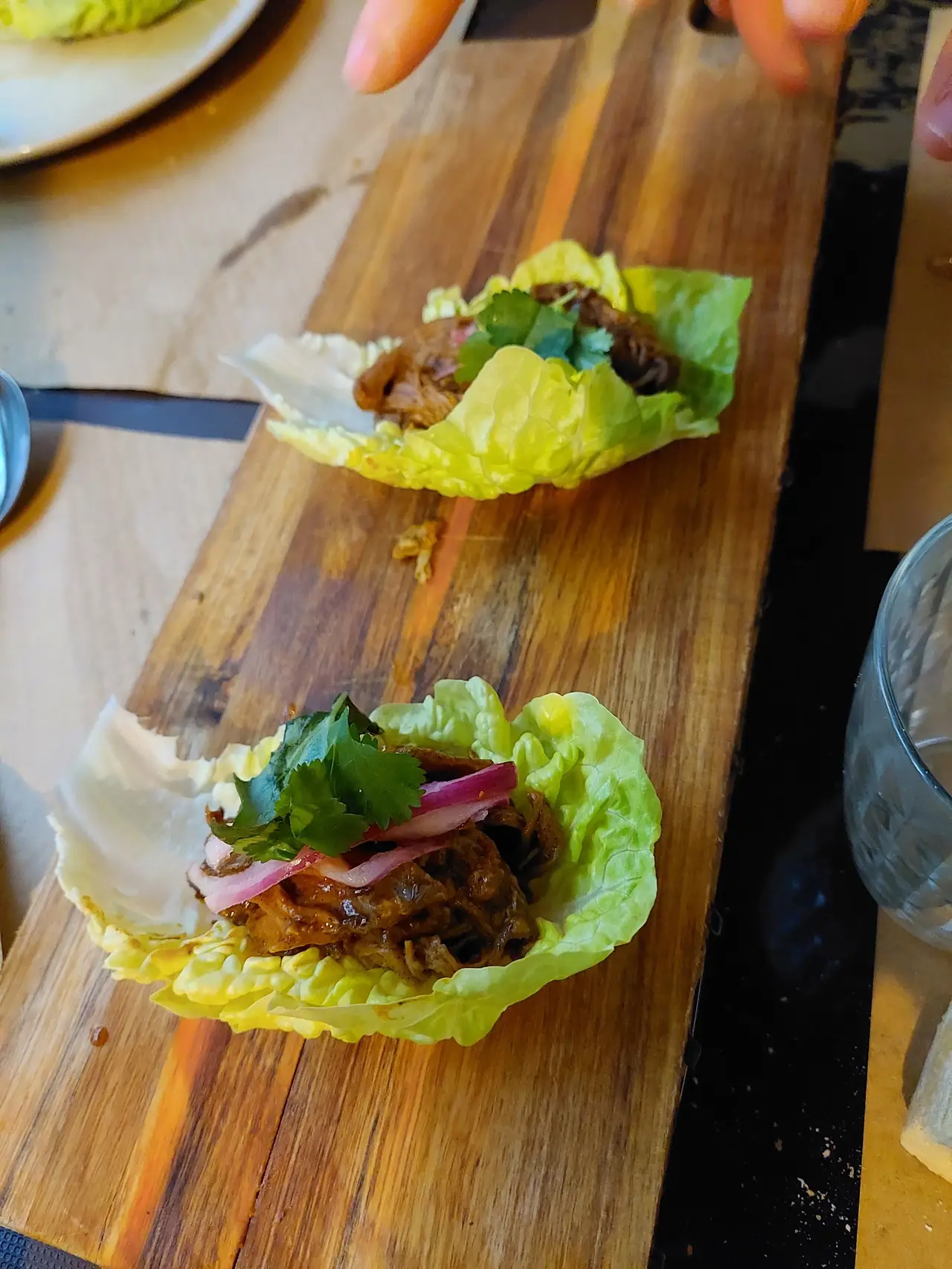 Two lettuce cups filled with braised meat, pickled red onion and cilantro on a wooden board