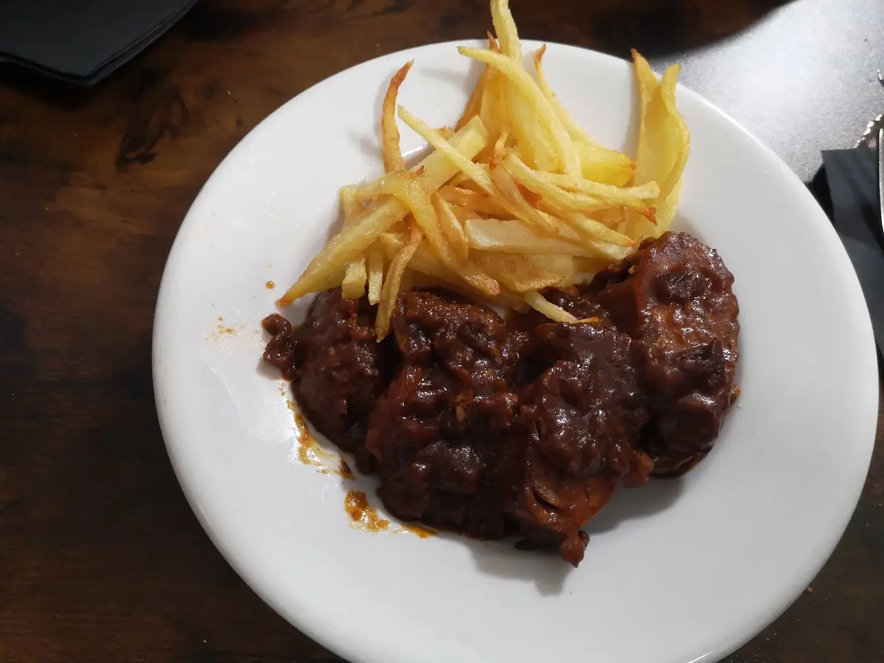 Plate of braised meat in dark sauce with a side of thin-cut fries