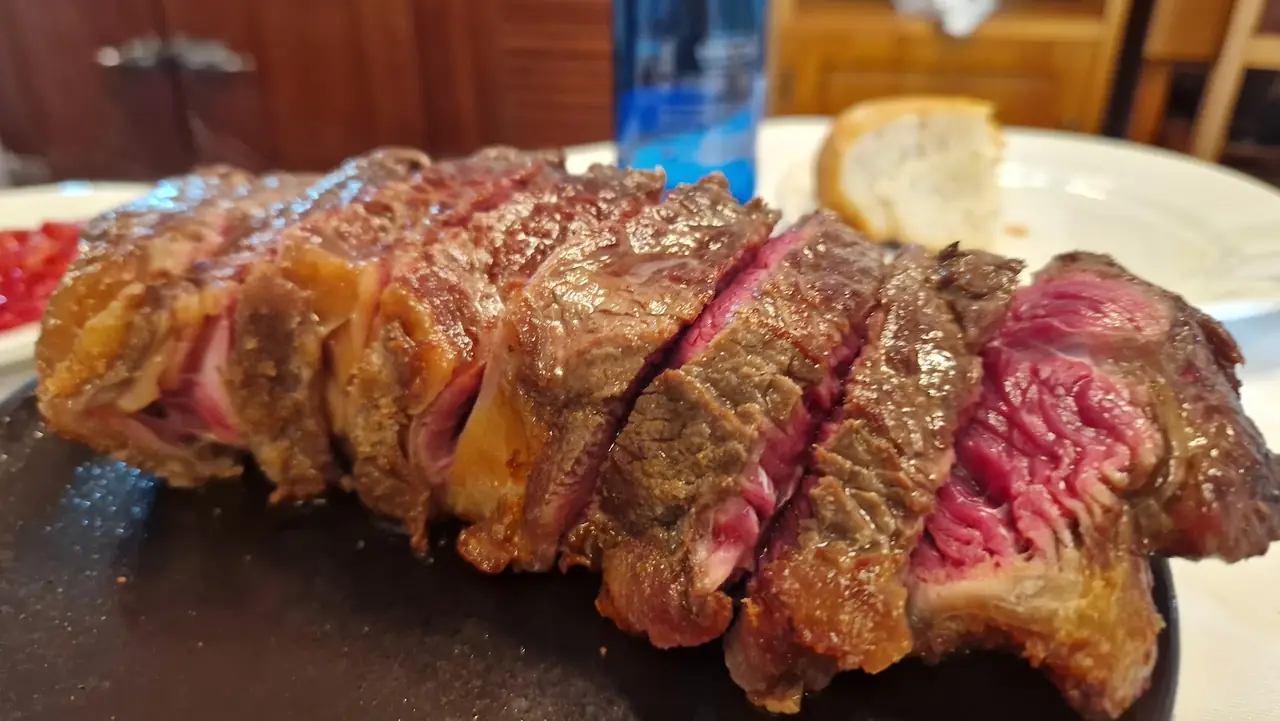Sliced grilled steak served rare on a black board, with bread in the background