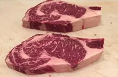 Two raw, well-marbled beef steaks displayed on a wooden board