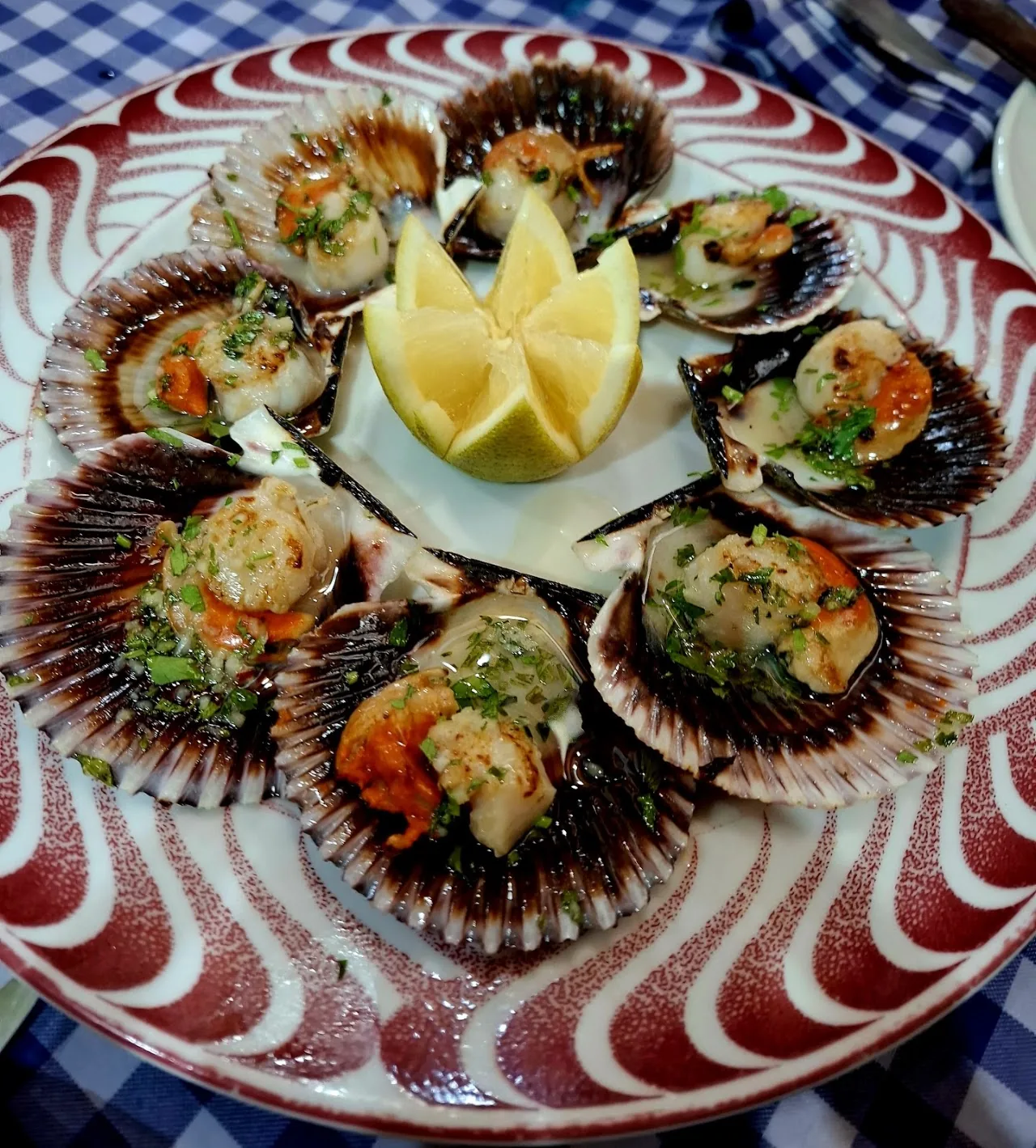 A plate of stuffed scallop or clam shells arranged around a lemon wedge and parsley garnish