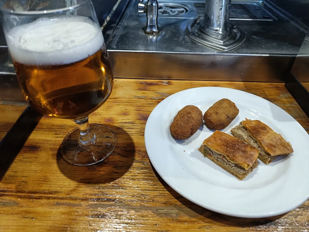 A glass of beer beside a plate of croquettes