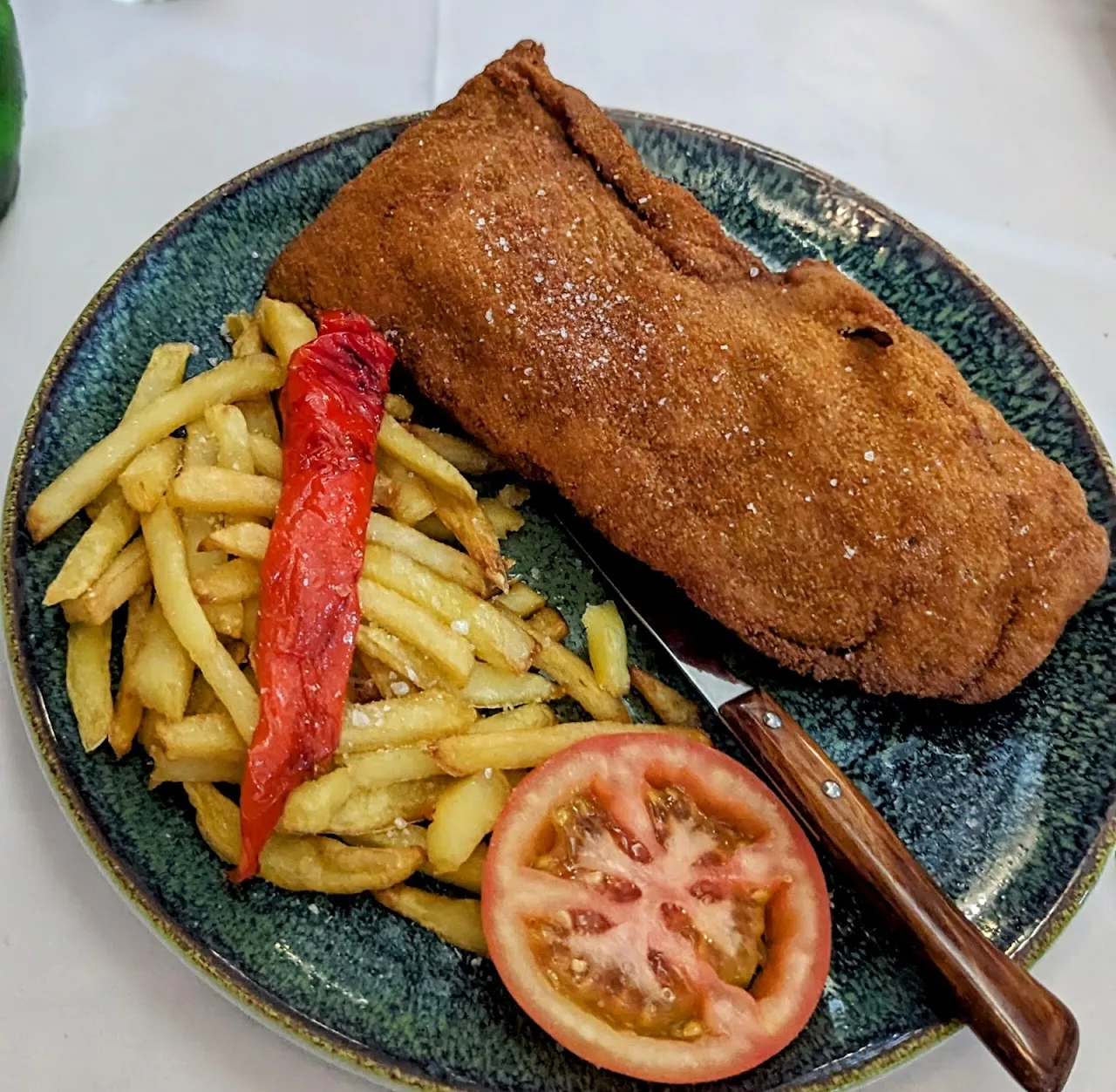 A breaded cutlet with french fries, a roasted red pepper, and tomato slices