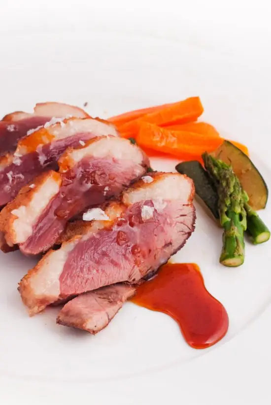 Sliced duck breast with roasted carrots, asparagus and zucchini in a red pan sauce