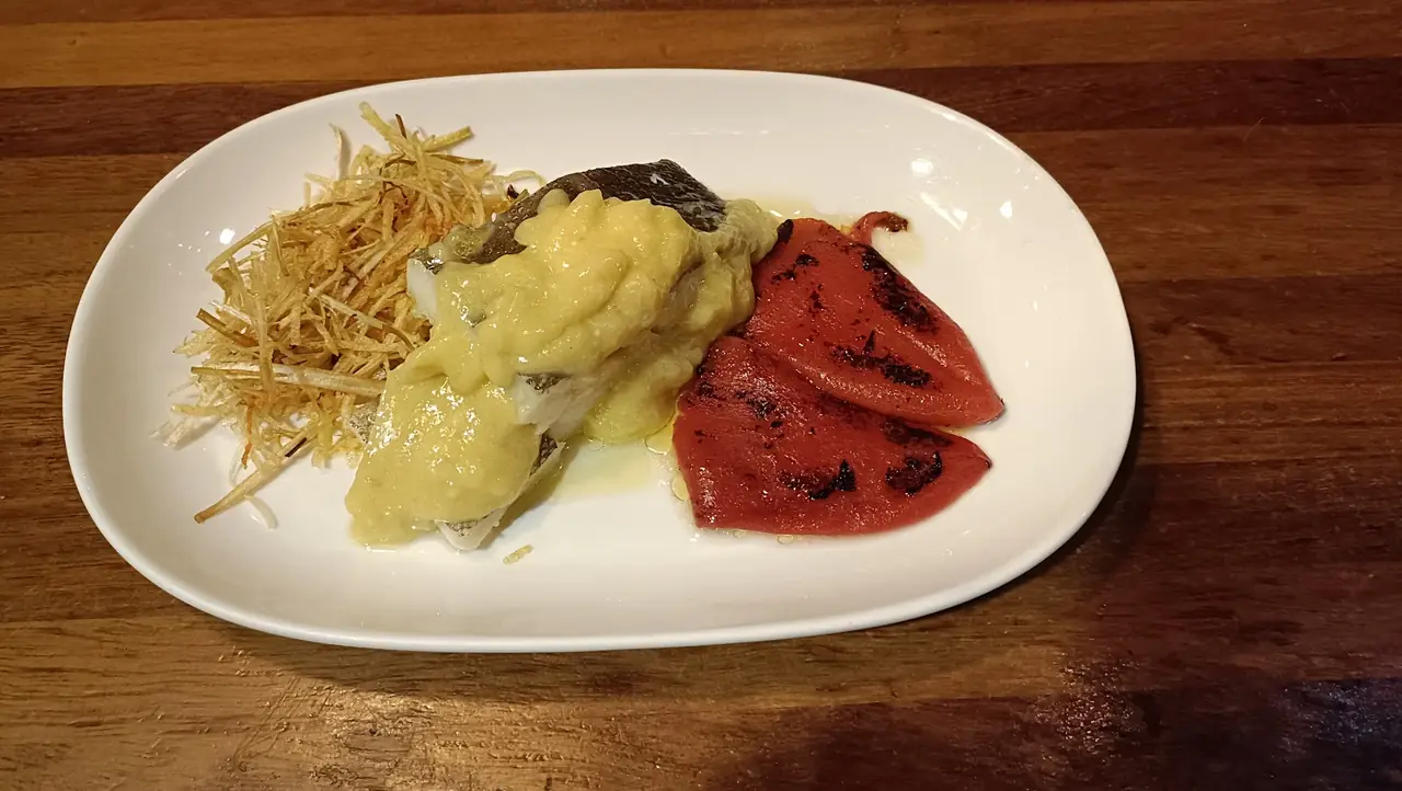 Fish fillet with garlic sauce, roasted red pepper strips and shoestring fries on an oval plate