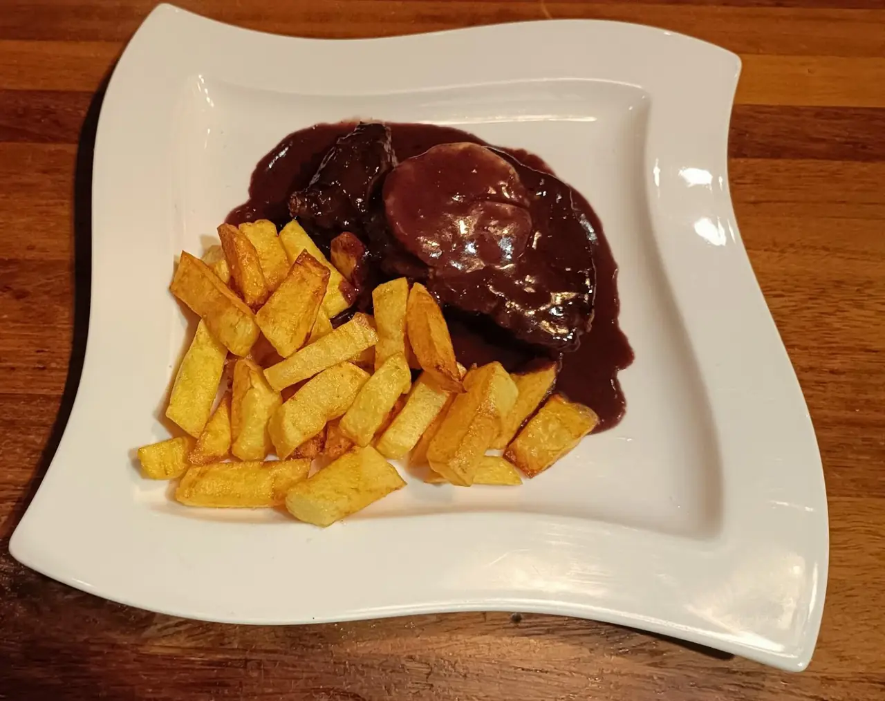 Meat in a dark red wine sauce with hand-cut fries on a square plate