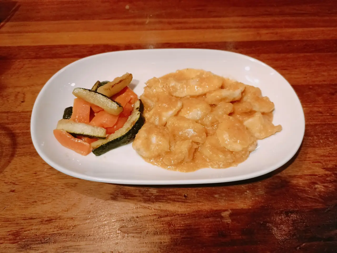Battered seafood in a light orange sauce with grilled carrot and zucchini on an oval plate