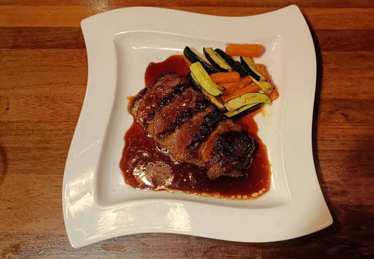 Grilled steak in a dark sauce with sauteed carrot and zucchini batons on a square plate