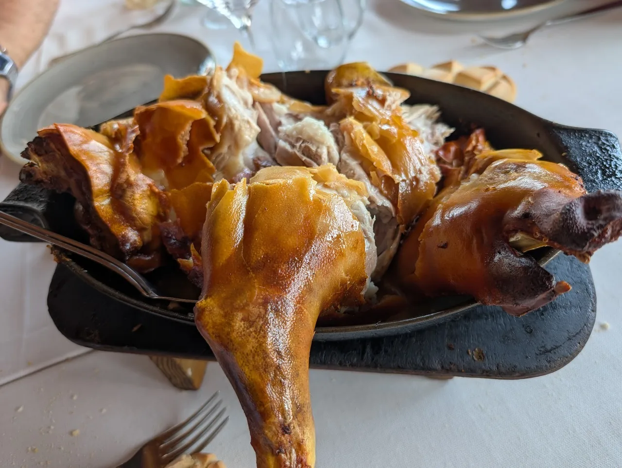 A roasted suckling pig on a black plate with pan juices