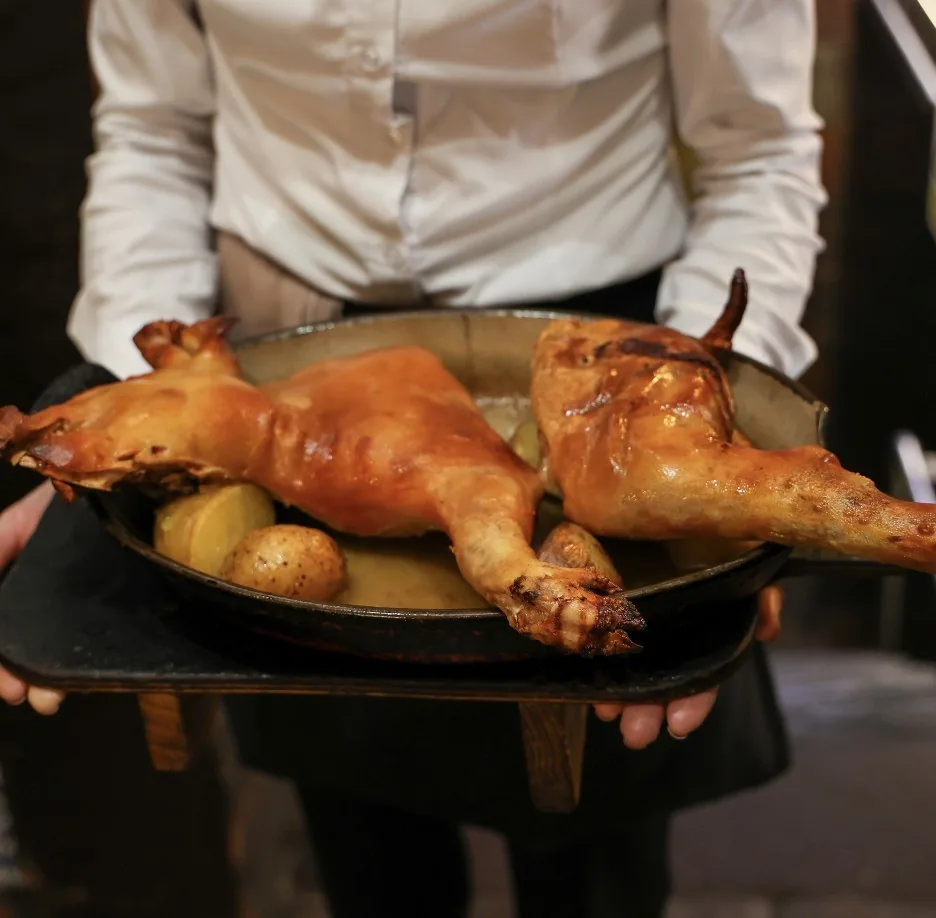 A waiter carrying a tray with a whole roast suckling pig and potatoes