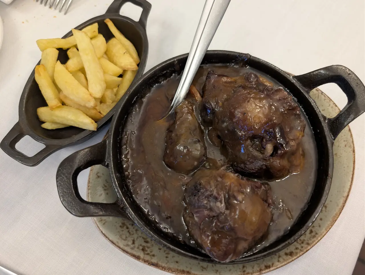 Braised meat in dark sauce in a small cast iron pot beside a dish of thick-cut fries