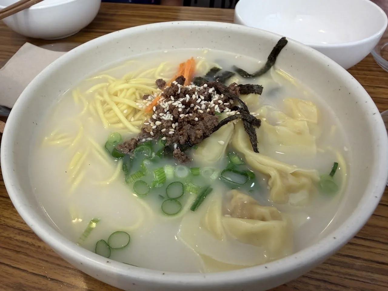 A bowl of noodle soup topped with seaweed strips, green onion and sesame seeds