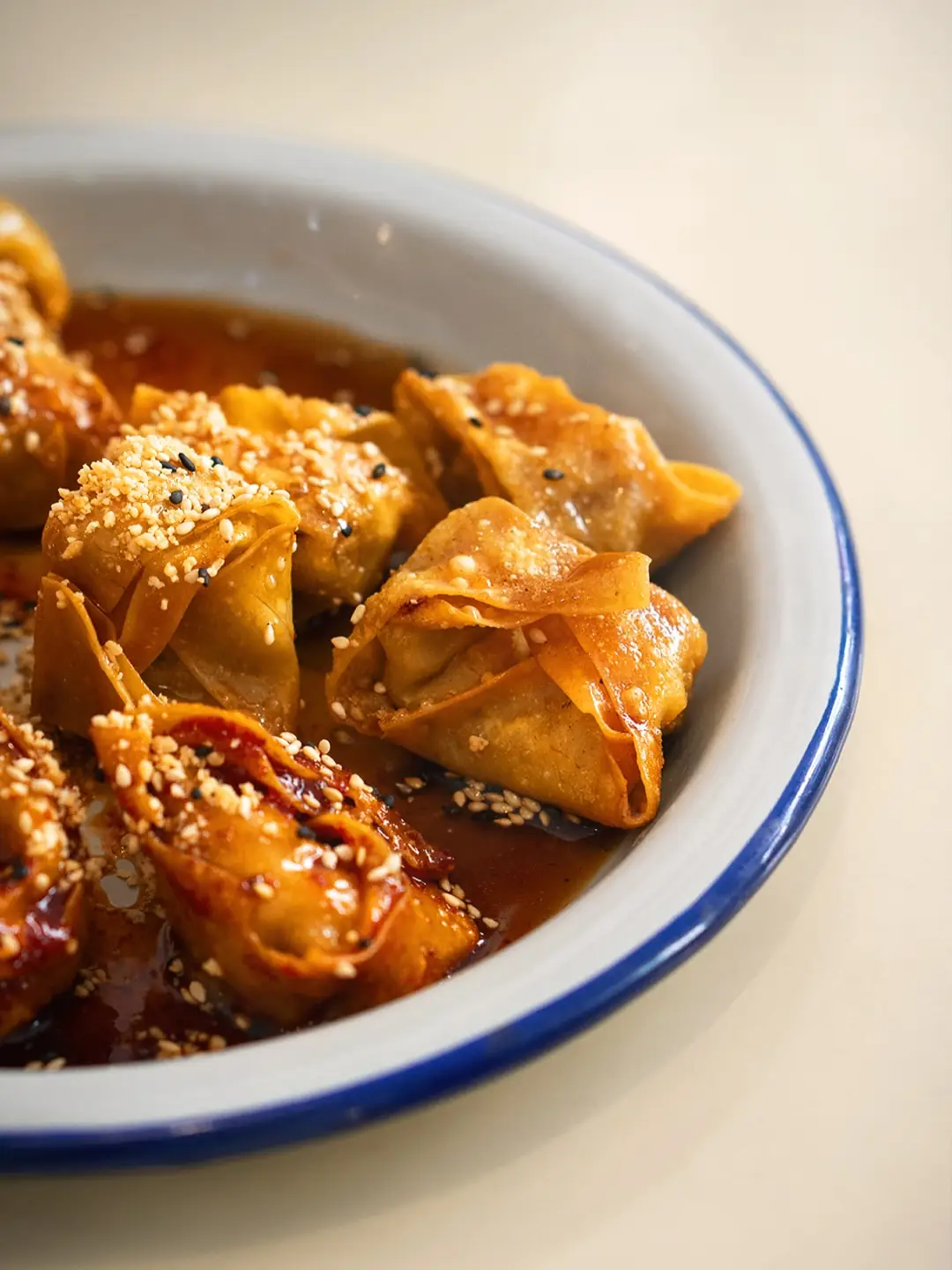 Crispy fried dumplings glazed in chili sauce and topped with sesame seeds on a blue-rimmed plate