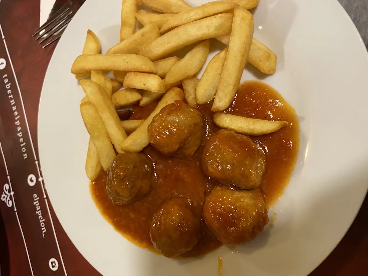 A plate of meatballs in gravy with french fries