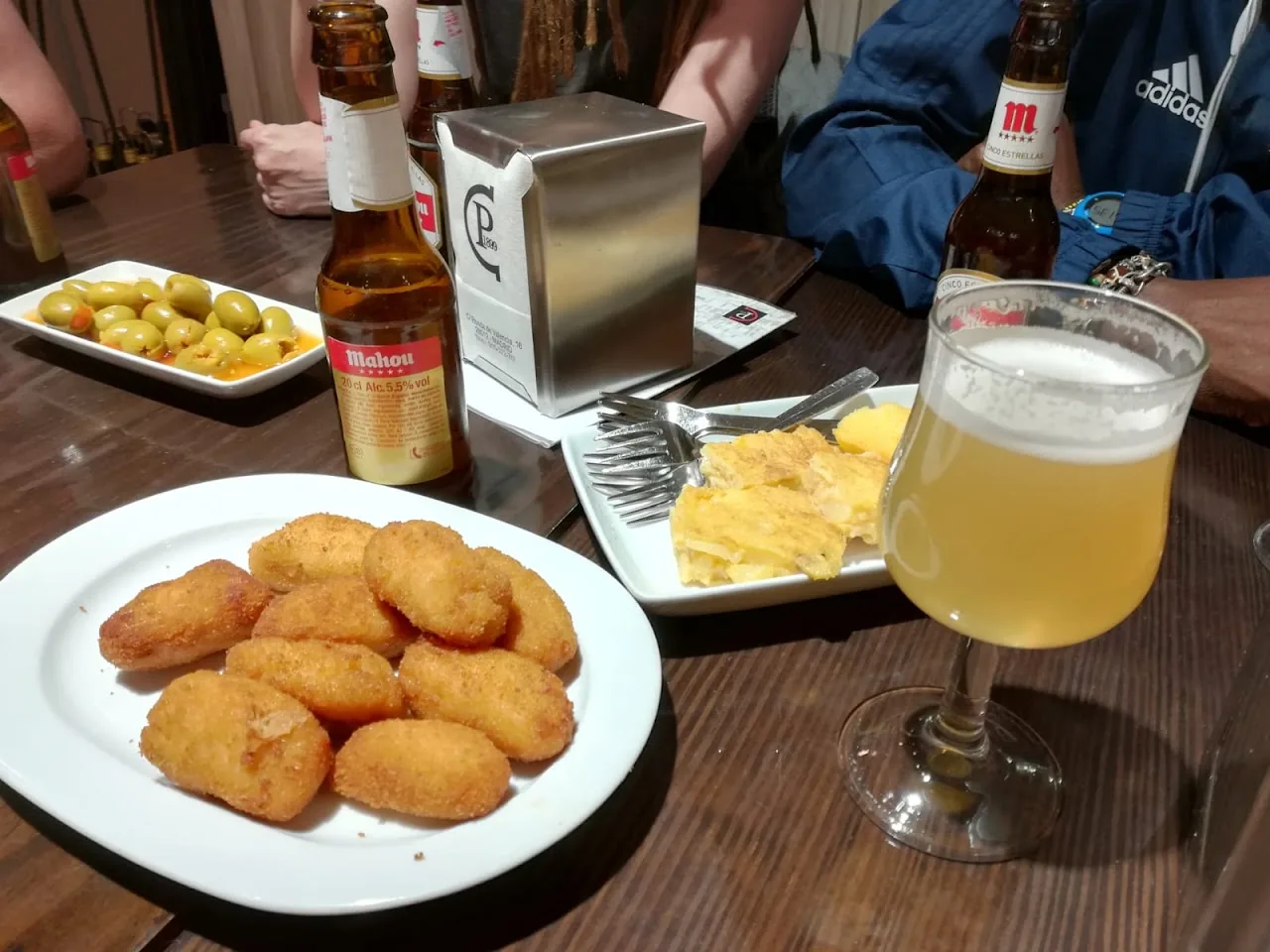 A plate of golden fried croquettes on the table next to a glass of beer and olives