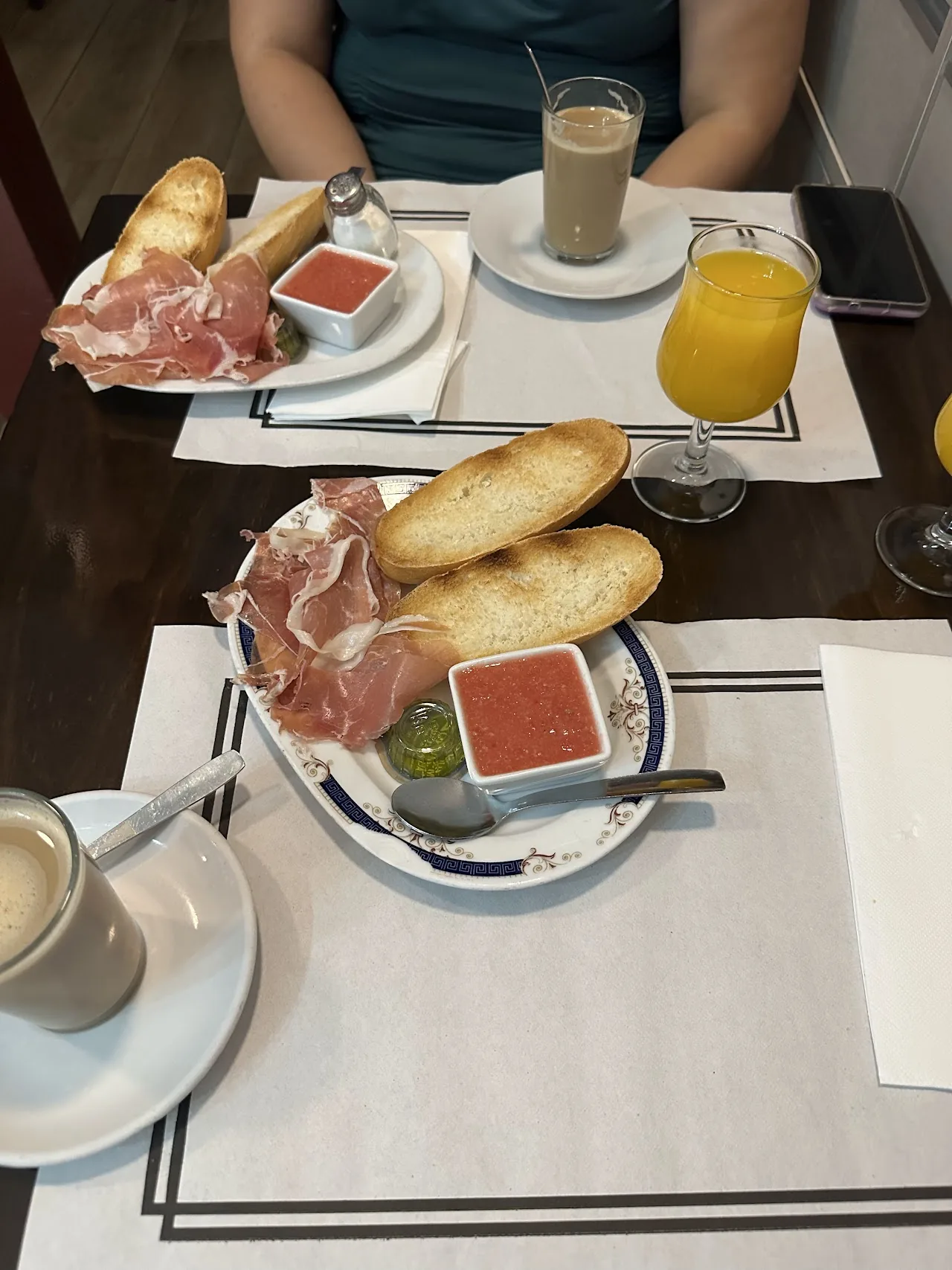 Two plates of sliced jamon serrano with bread, orange juice, and coffee