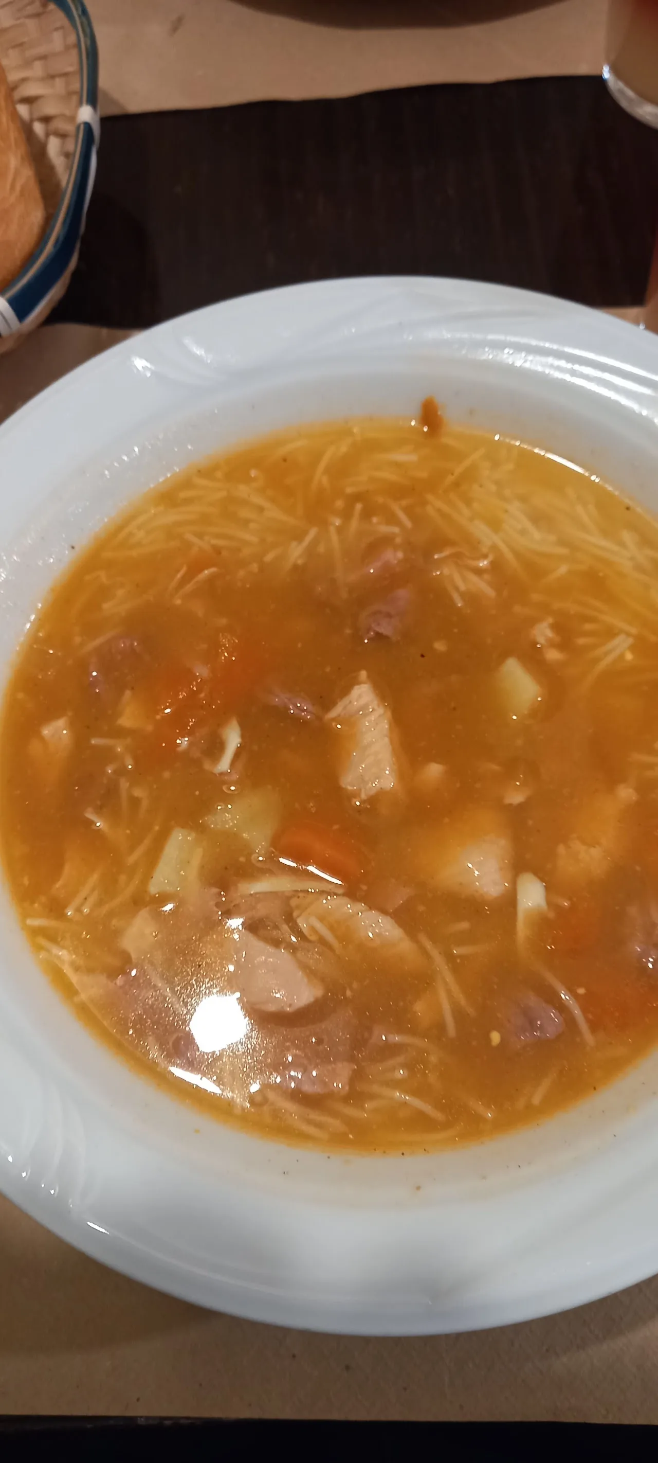 A bowl of broth soup with noodles and chunks of meat