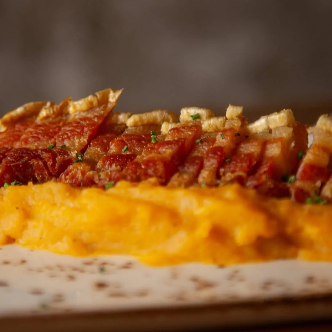 Sliced crisp cured pork over orange mash on a plate