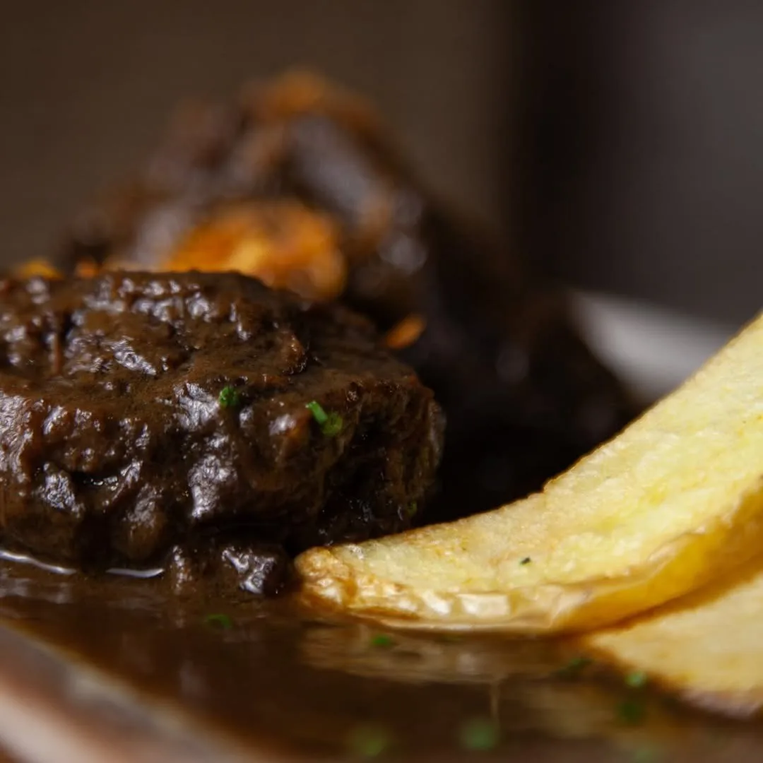 A piece of braised meat in dark sauce with a fried potato slice