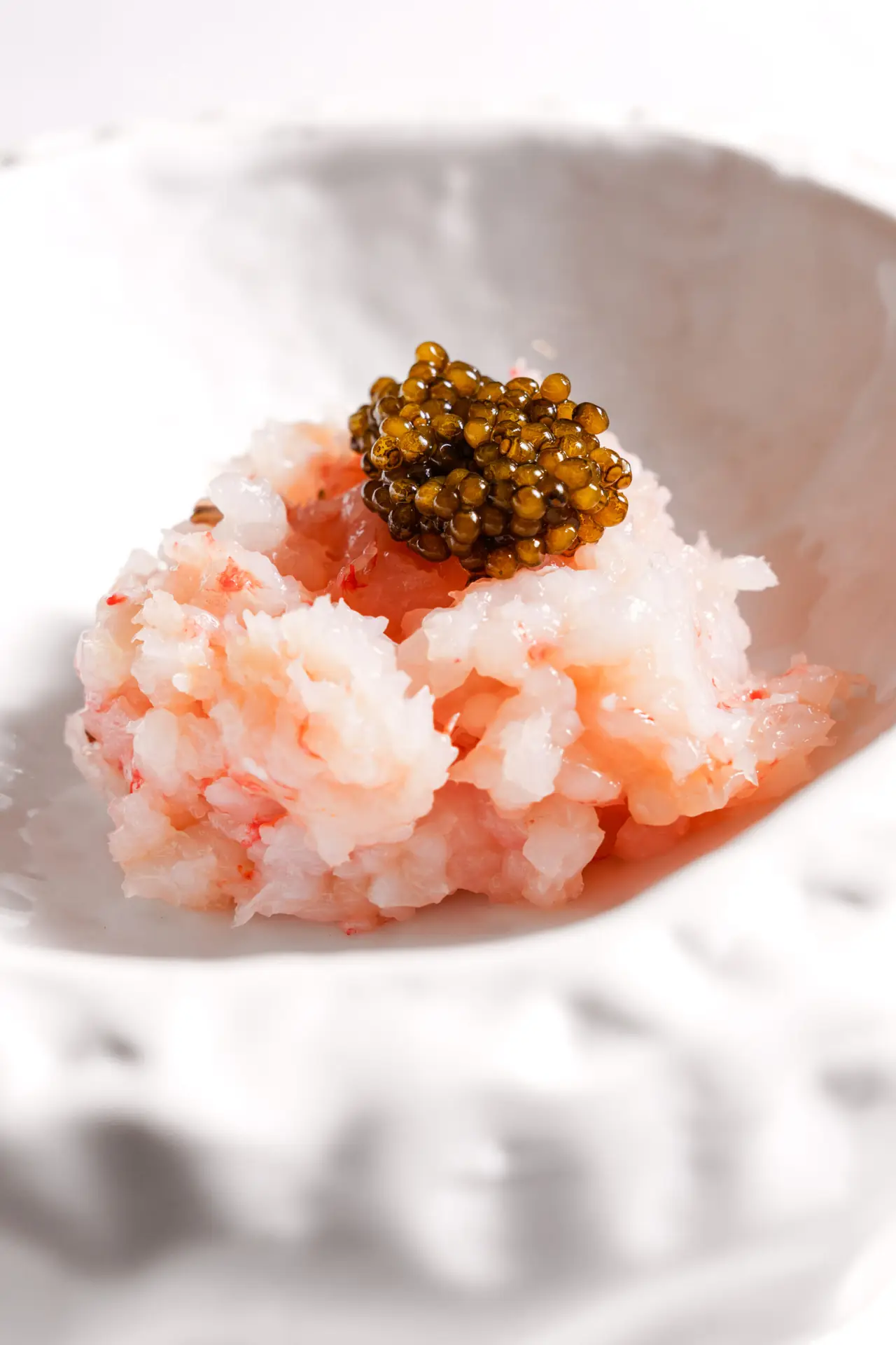 Chopped raw prawn tartare topped with a spoonful of golden caviar in a white ceramic bowl.