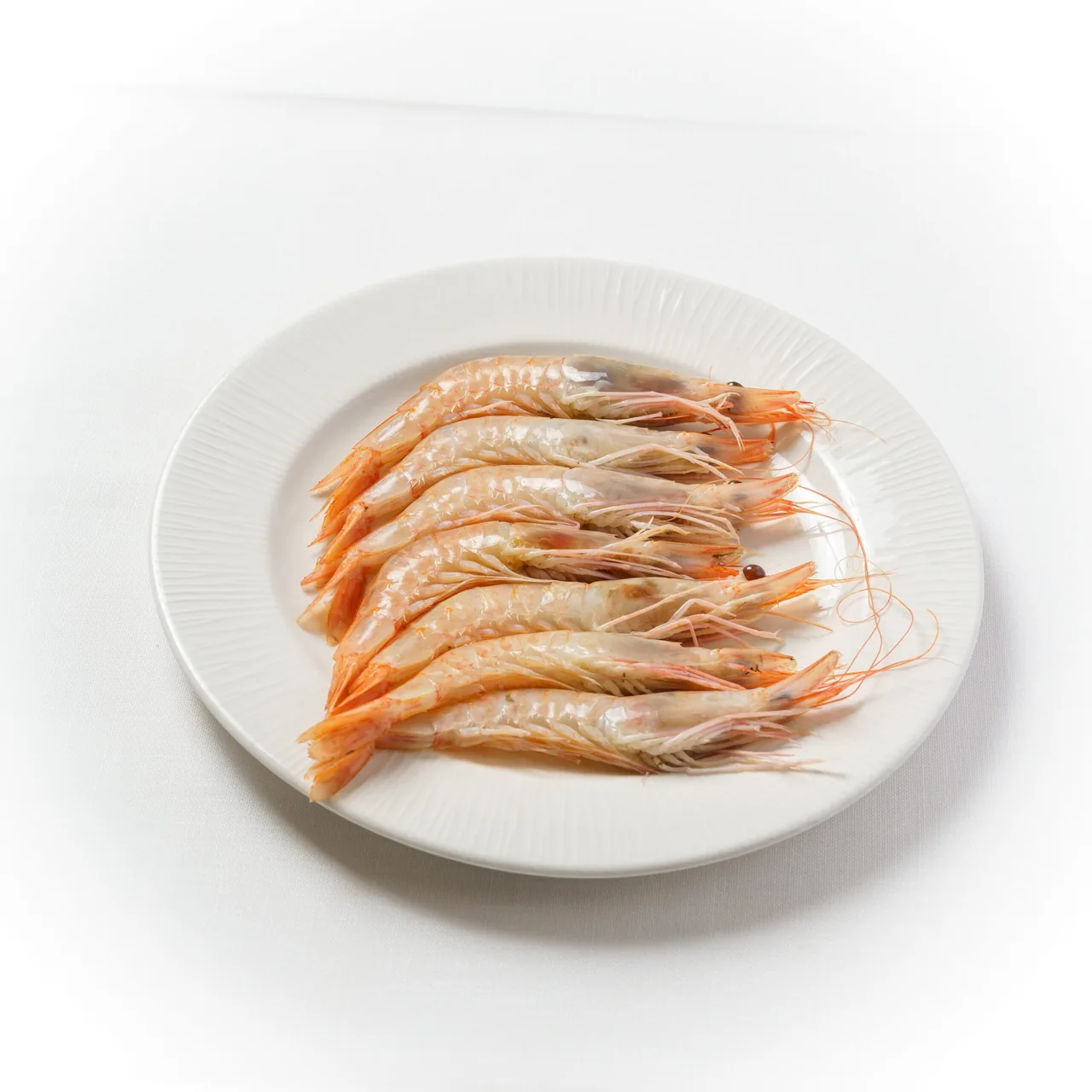 A white plate of peeled pink prawns arranged in a row