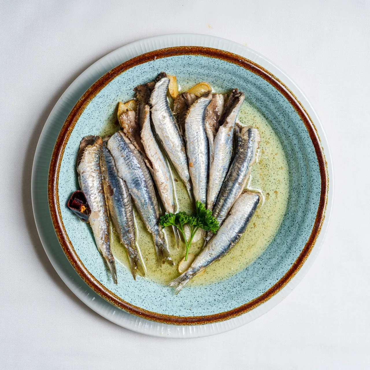 A blue plate of whole small fish in a pale sauce with a herb garnish