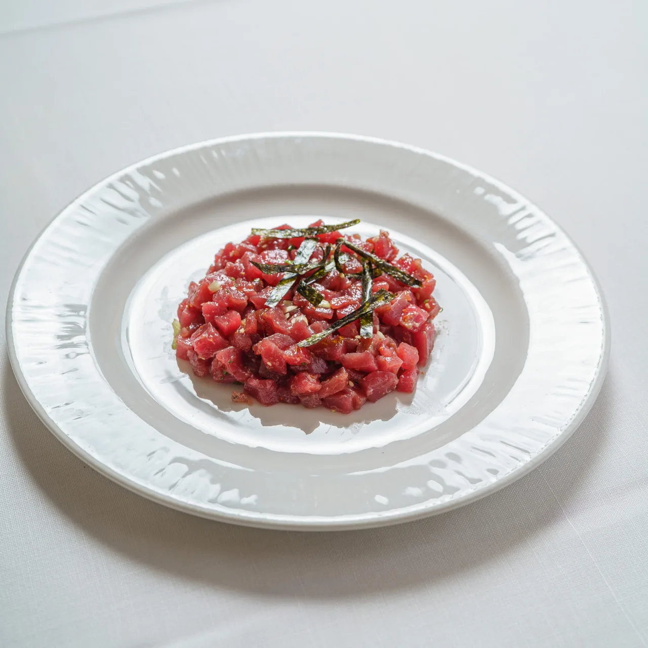 A mound of finely chopped red tartare with a thin green strand on a white plate