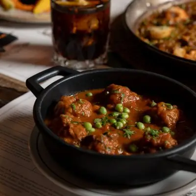 Meatballs in tomato sauce topped with peas and herbs, served in a black cazuela dish at Casa Rafols