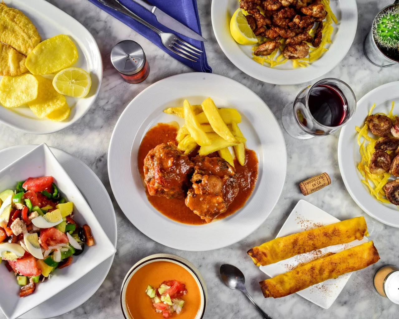 A table seen from above with several plates of stews, fries, salad and croquette-style dishes