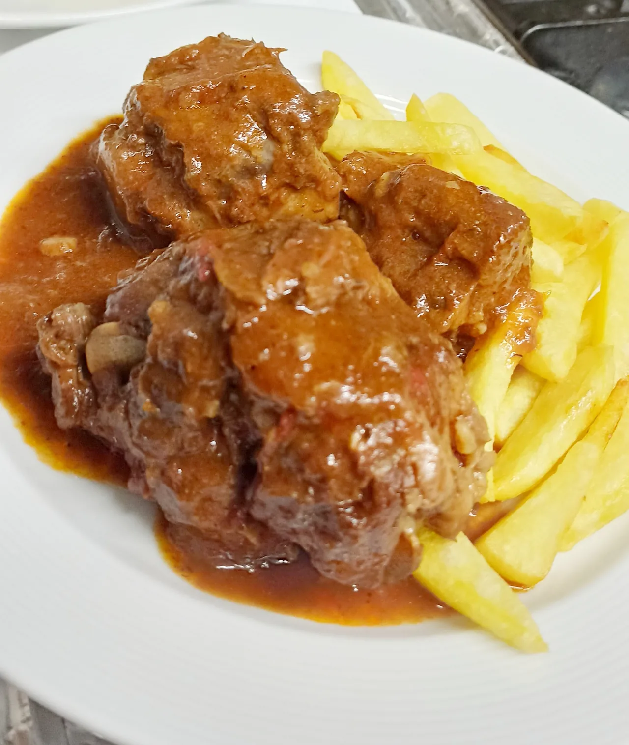 A plate of braised meat in brown sauce with fries