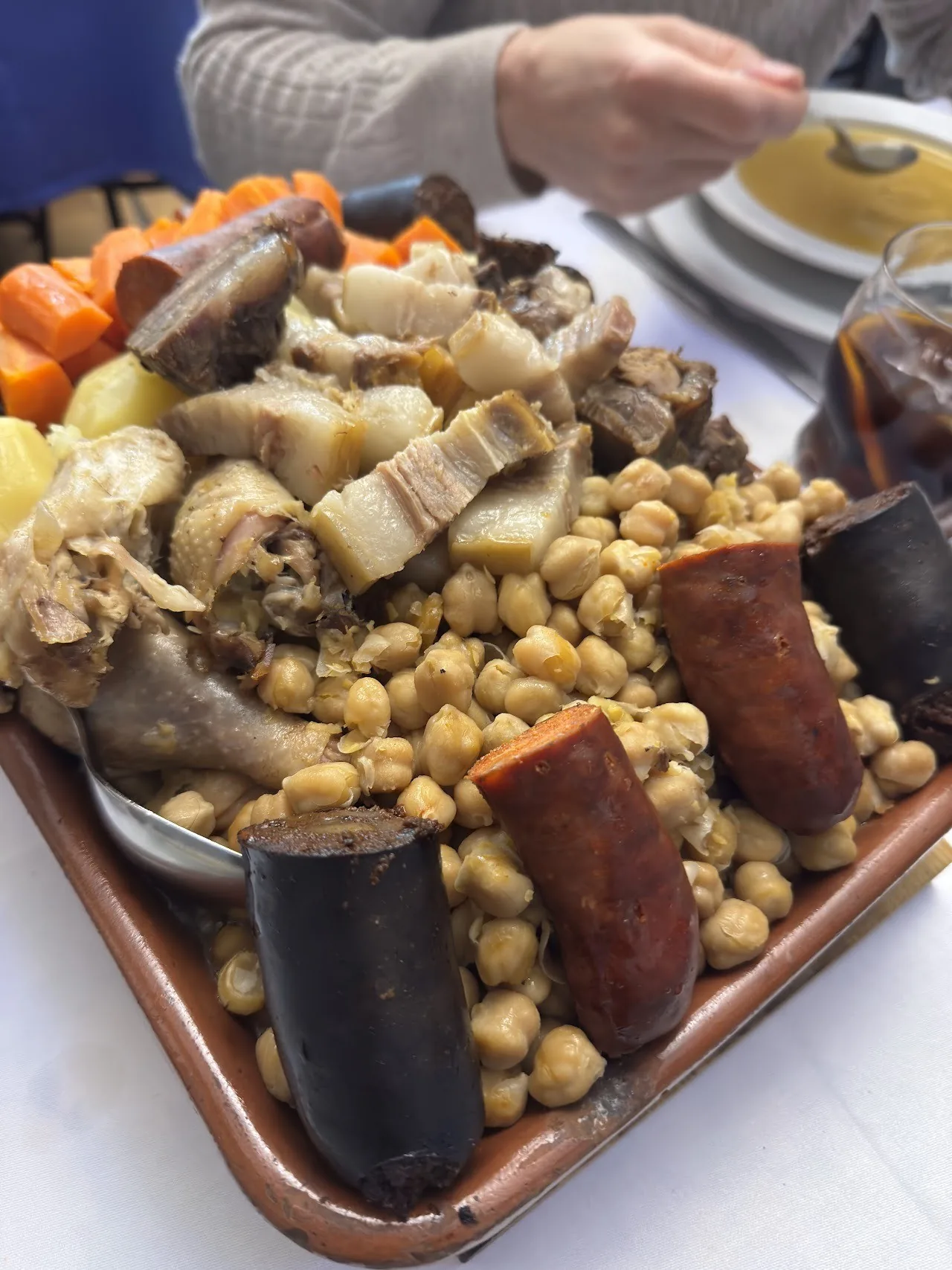 A brown tray of chickpeas with sausages and cuts of meat