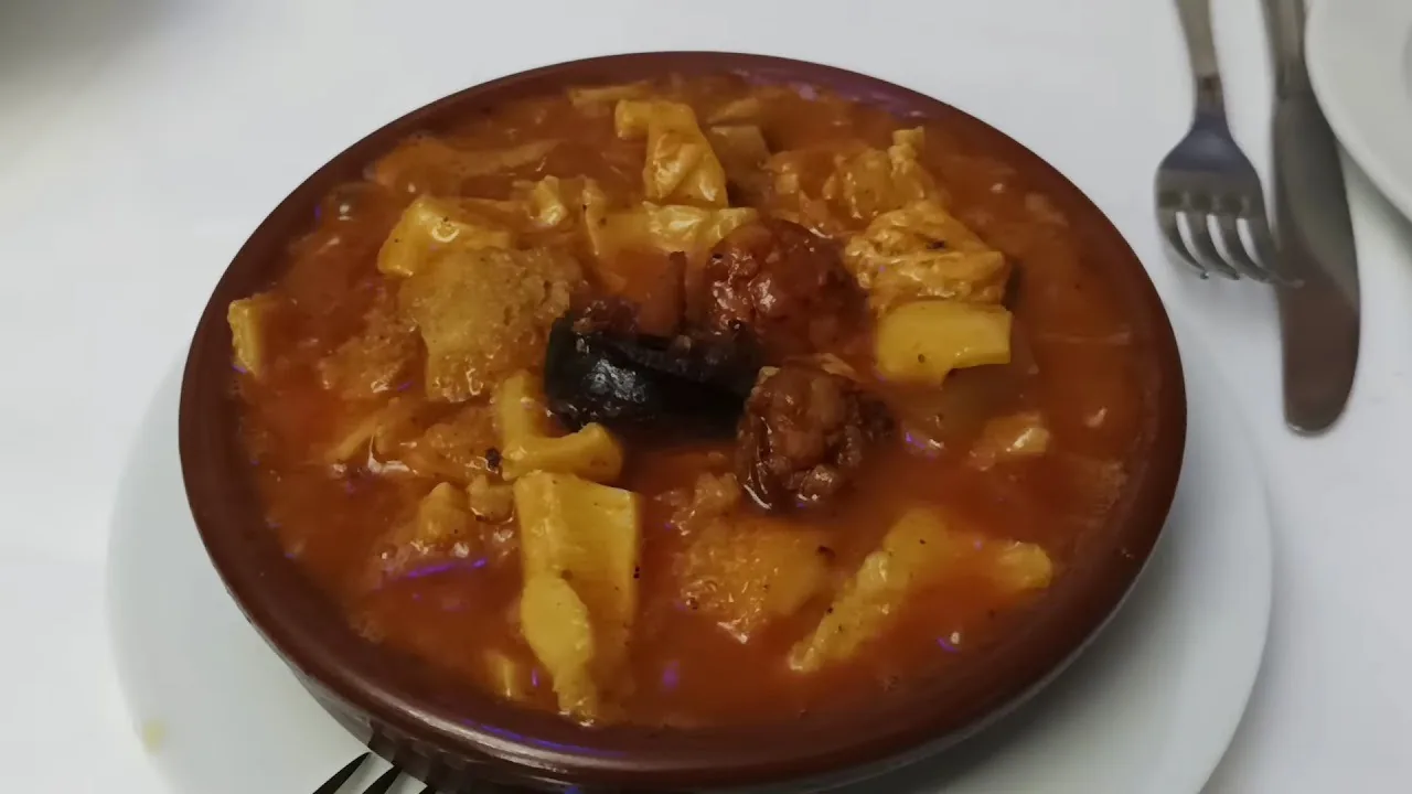 A round earthenware bowl of stew with a piece of chorizo