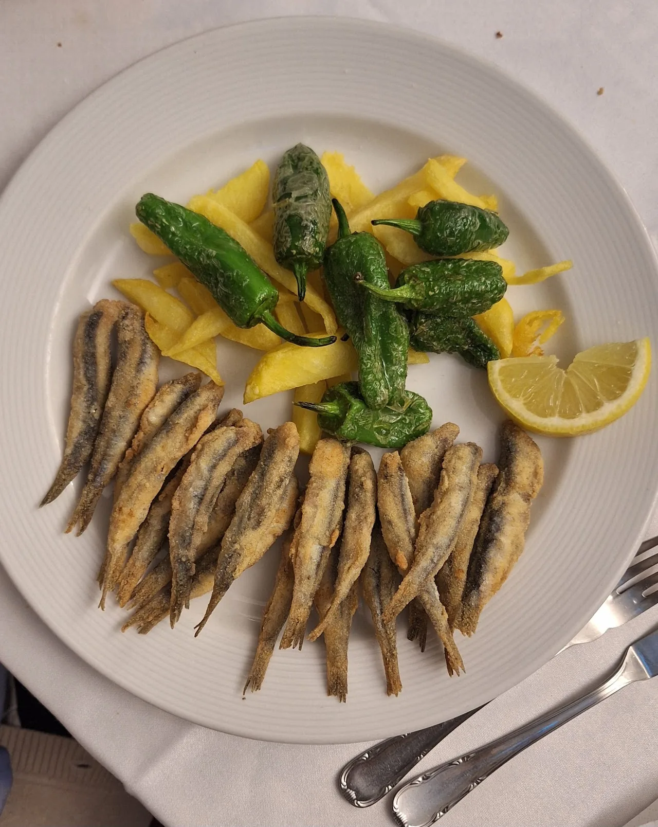 Fried anchovies (boquerones) with fried green peppers and a lemon wedge