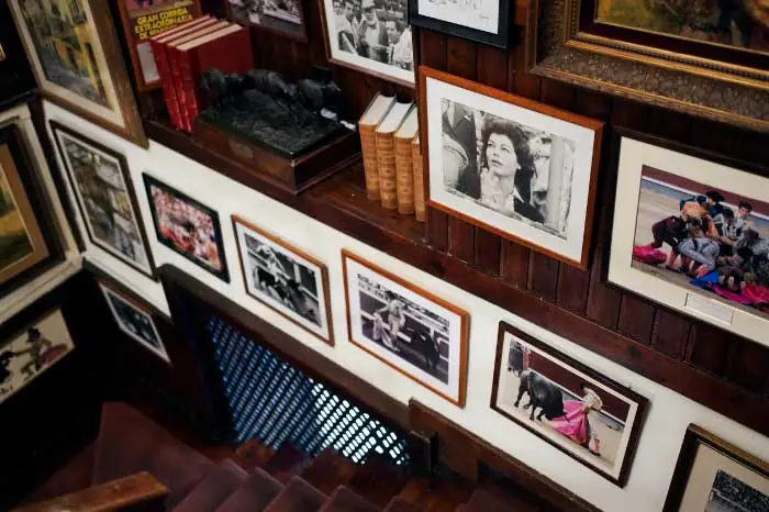 Restaurant stairwell with wooden panelling and walls densely hung with framed bullfighting photographs and prints