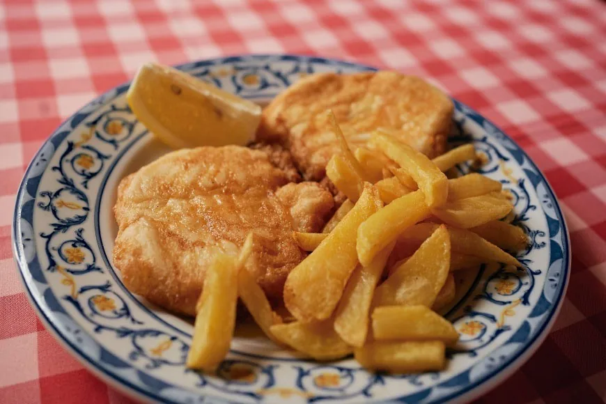 A breaded fillet with lemon and fries on a blue-and-white patterned plate