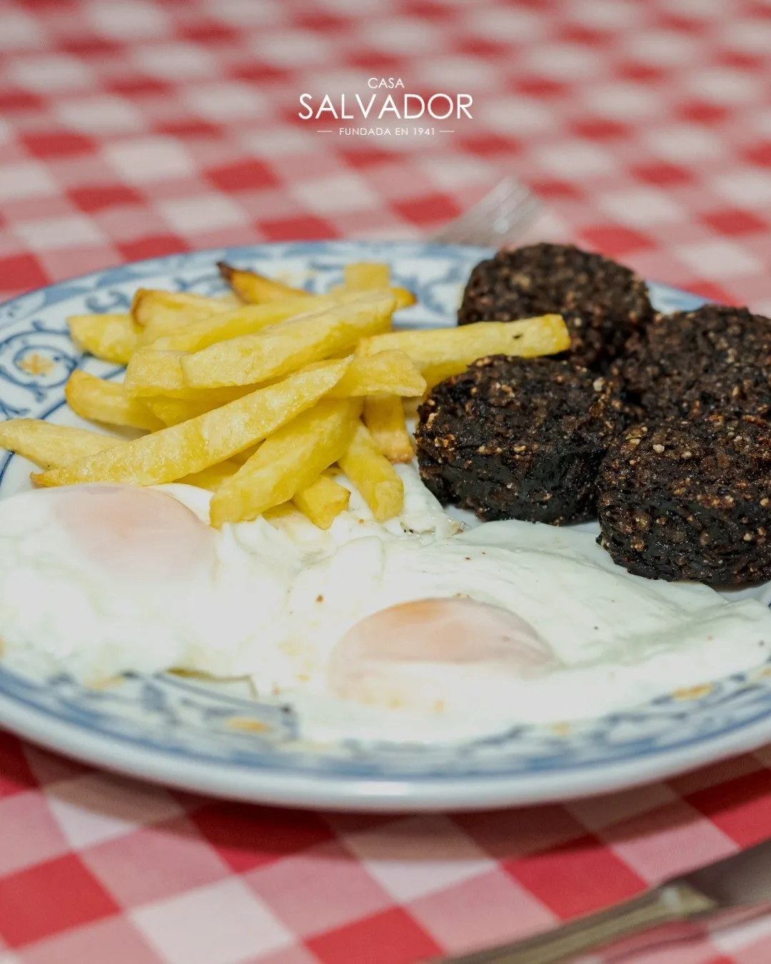 Fried eggs, chips and black sausage slices on a plate on a checked cloth