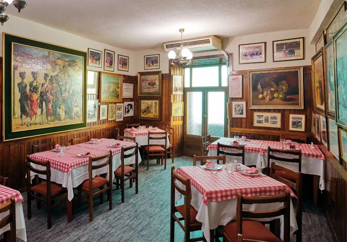 A dining room with checked tablecloths and walls covered in framed pictures