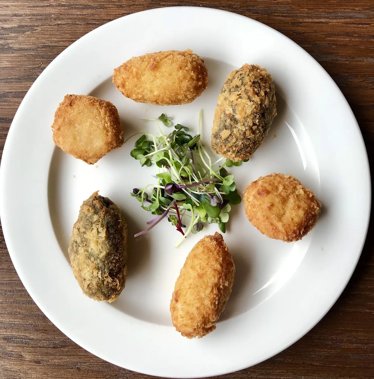A plate of assorted croquettes with a garnish of microgreens