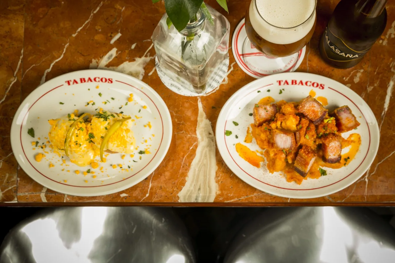 Two white plates of hot dishes on a marble table next to a glass