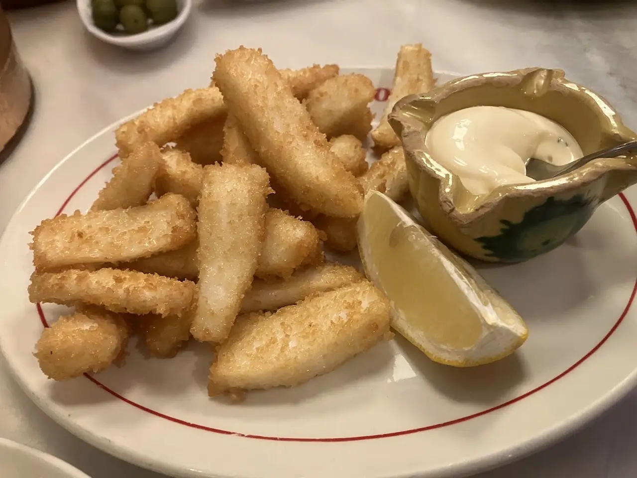 Fried breaded fish strips with a lemon wedge and a garlic mayonnaise dip.