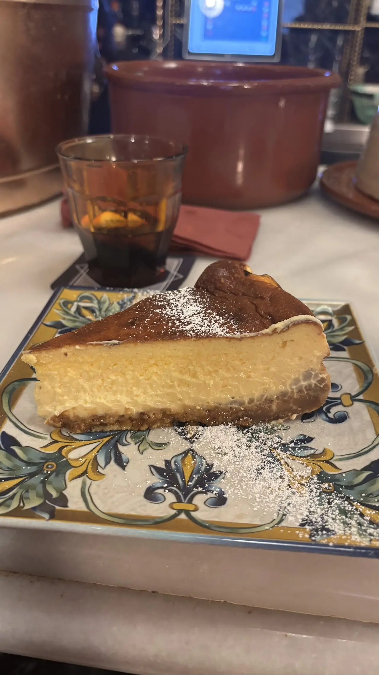 A slice of cheesecake dusted with powdered sugar on a patterned plate.