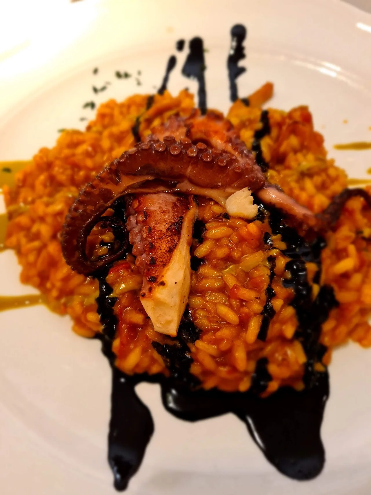 Rice dish topped with grilled octopus and a squid-ink drizzle